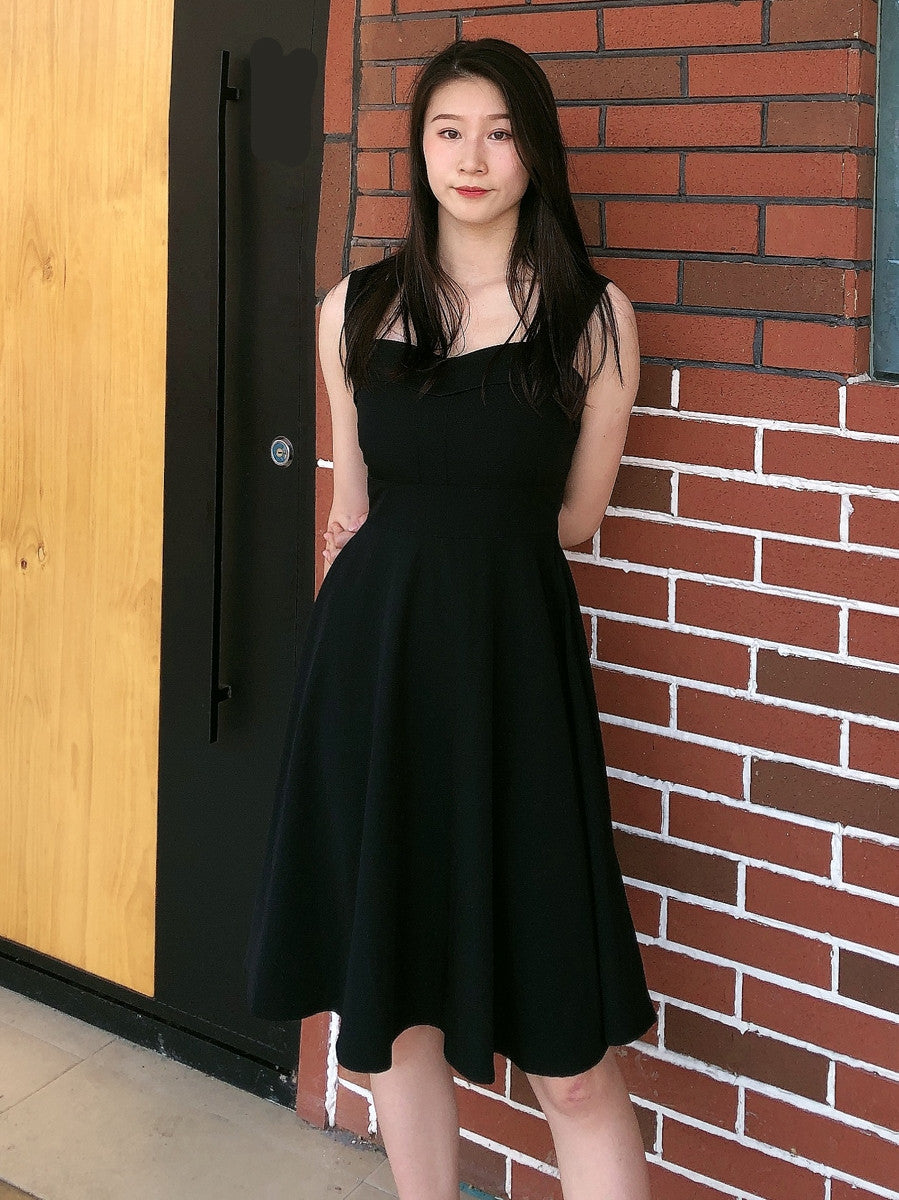 Woman in a black dress standing against a brick wall.