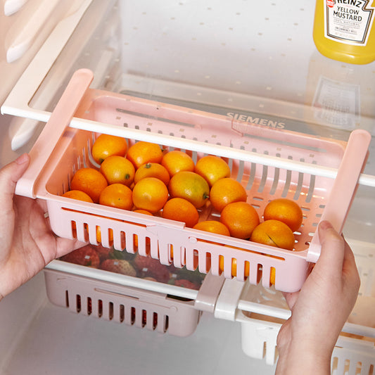 Pink fruit organizer with oranges inside, held by a person in front of an open refrigerator.