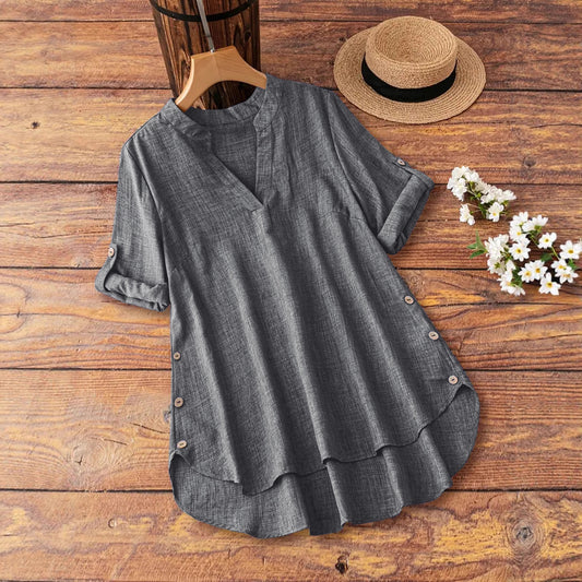 Gray blouse on a wooden surface with a straw hat and white flowers.